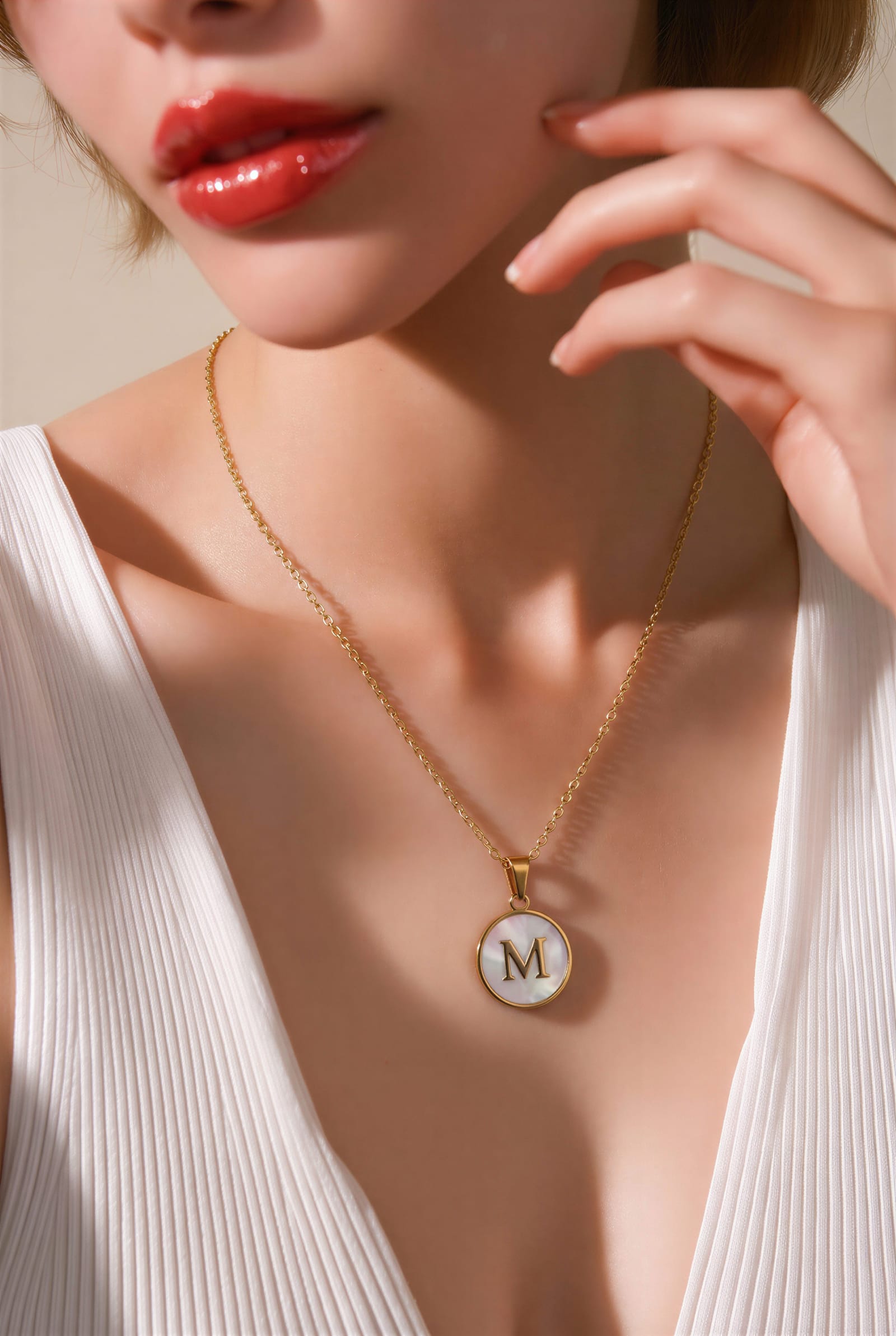 A white shell initial pendant on a fine gold chain, worn at the collarbone